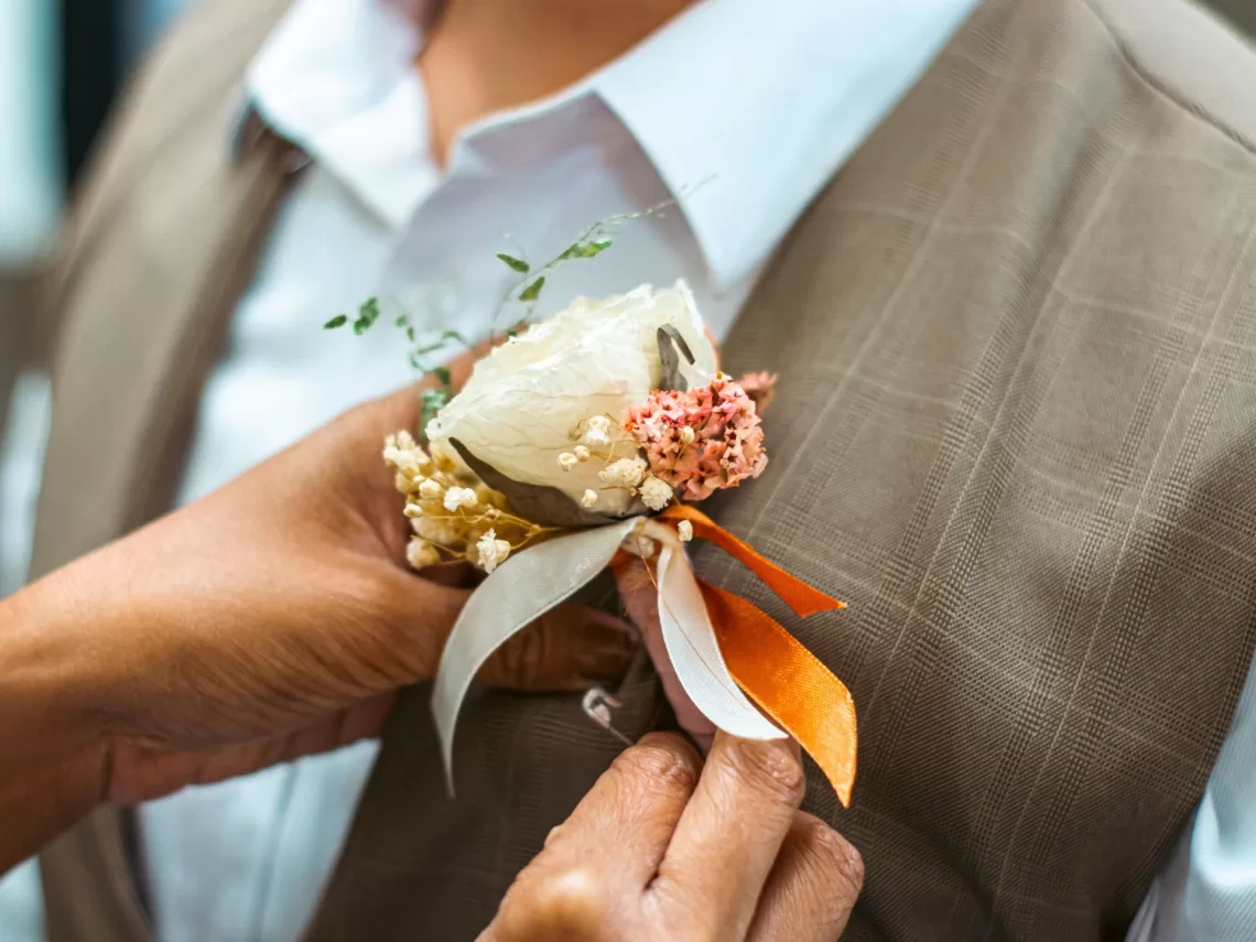 A woman putting on the groom's wedding boutonniere.