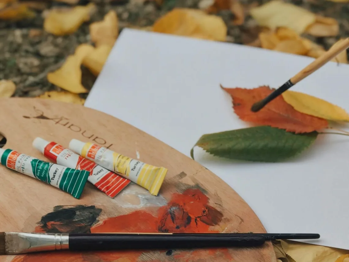 Canvas and paints sitting on top of a pile of leaves.